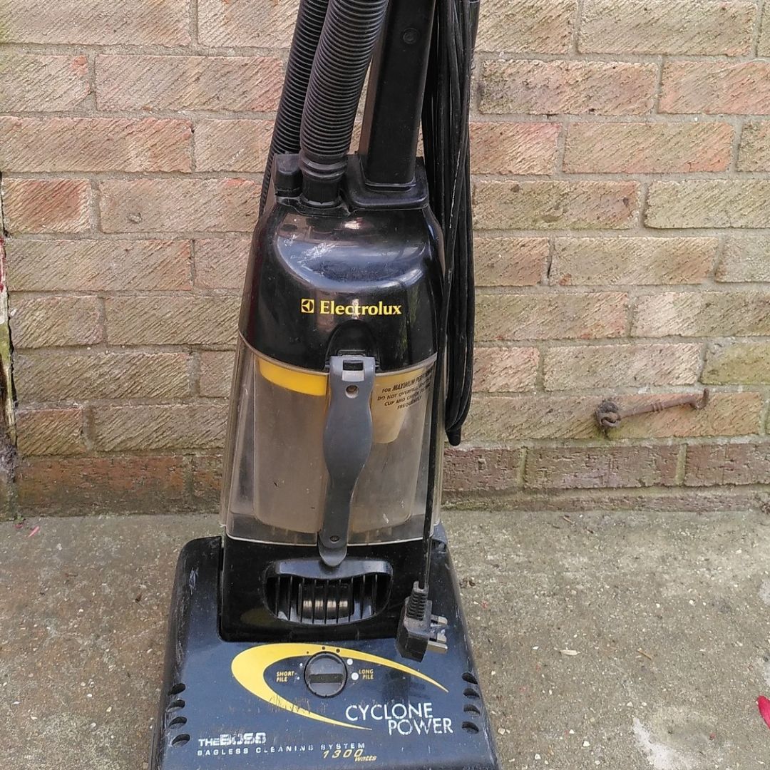 Electrolux Vacuum Repairs 2 A black Electrolux Cyclone Power 1300 bagless vacuum cleaner, showing some signs of use, is positioned against a brick wall outdoors. The vacuum's dust container is partially visible.