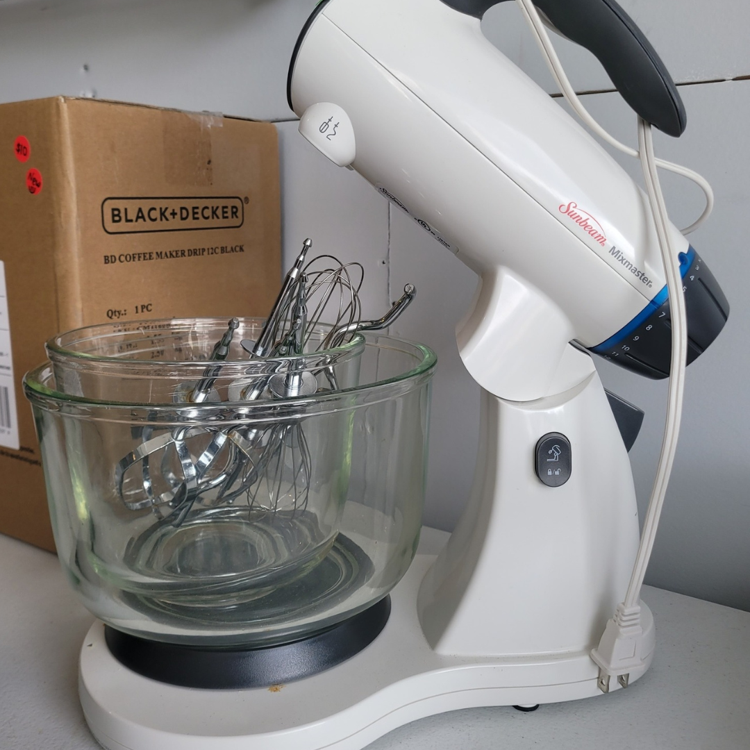 sunbeam-mixer-repair2 Sunbeam Mixmaster stand mixer, primarily white with gray and blue accents. The mixer's beaters are in a clear glass bowl that sits on the mixer's base. A Black & Decker coffee maker box is visible in the background.